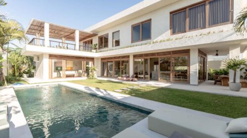 Modern luxury villa with an outdoor pool, spacious patio, and large glass doors, surrounded by greenery and bathed in natural sunlight.